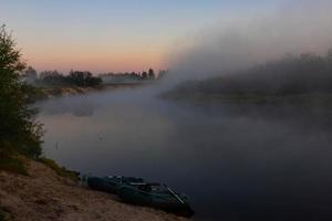 Zwei Gummiboote mit Angelausrüstung am frühen Morgen während des Nebels, geparkt am Ufer des Flusses. foto