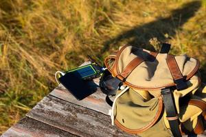 Solarbatteriegerät, Powerbank und Telefon auf einem Holztisch mit Rucksack. Laden Sie Ihr Smartphone mit Solarenergie auf. selektiver Fokus foto