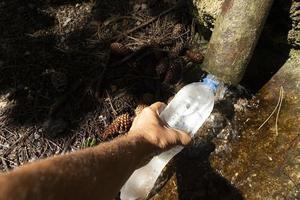 Hand hält eine Flasche und füllt sie mit Wasser aus einem natürlichen Bach foto