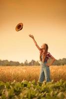 glückliches aufgeregtes Bauernmädchen, das ihren Hut in Feld vt wirft