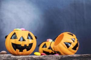 Halloween-Kürbis-Gesichtseimer mit bunten Süßigkeiten im Inneren auf alten Holzbrettern über blauem Hintergrund mit Farbverlauf foto