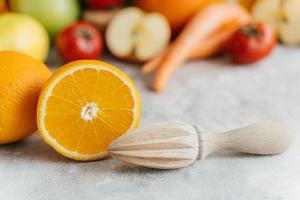 in Scheiben geschnittene Orangen- und Holzpresse vor verschwommenem Obst- und Gemüsehintergrund. Auspressen von frischen Zitrusfrüchten. gesundes ernährungskonzept foto