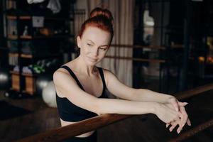hübsche junge rothaarige Frau, die sich auf die Ballettstange stützt foto