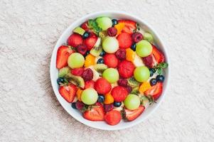 gesunder frischer obstsalat in der schüssel. scheiben von erdbeere, himbeere, kiwi, mandarinen, blaubeere auf teller. leckere Früchte. vegetarisches Gericht. reife Beeren. foto