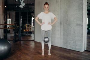 Sportliche rothaarige Frau, die einen Mini-Pilates-Ball mit den Knien hält foto