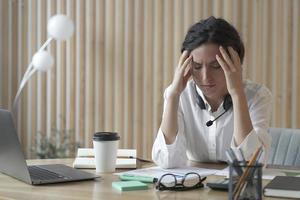 müde spanische geschäftsfrau mit geschlossenen augen, die am arbeitsplatz im büro sitzt und unter kopfschmerzen leidet
