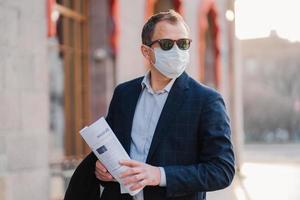 geschäftsmann trägt schutzmaske gegen übertragbare infektionskrankheiten, liest zeitungen, elegant gekleidet, posiert im freien, denkt darüber nach, wie man neues coronavirus aus china verhindert. Grippe in der Stadt. foto