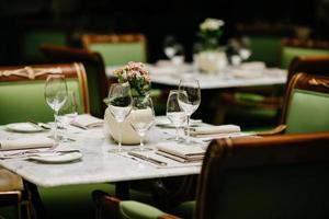 Horizontale Aufnahme eines quadratischen Tisches, serviert mit leeren Gläsern, Servietten, Tellern, Gabeln und Messern ohne Teller, grüne Stühle herum. gemütliches Restaurant oder Café foto