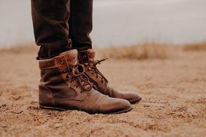 Seitlicher Schuss eines Mannes in zotteligen braunen Schuhen auf einer Liegefläche. Paar Stiefel auf Sand. Männchen hat einen Spaziergang im Freien in alten Schuhen. foto