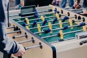 Zugeschnittenes Bild von aktiven Menschen spielen Kicker oder Tischfußball, wollen Erfolg haben und gewinnen, bevorzugen Sportspiele. Kickertisch mit gelben und blauen Plastikspielern foto