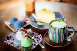 Matcha-Grüntee obenauf dekorierte Latte Art mit herzförmigem Milchschaum in einer bunten Tasse mit Mochi gefüllt mit Erdbeeren in einer Kachelschale auf Holztisch. foto