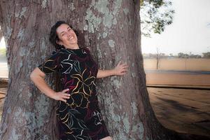 Reife Dame im Park an einem sonnigen Tag amüsiert sich gegen einen Baum stehend. foto