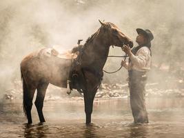 Ein junger Cowboy ruhte sich mit einem Pferd im Bach aus, nachdem er das Pferd geduscht hatte foto