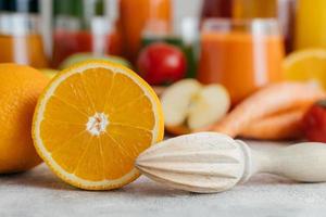 in Scheiben geschnittene frische Orange mit Squeezer. Saft aus frischem Obst herstellen. orange Farbe. verschwommene Saftgläser im Hintergrund. horizontaler Schuss foto