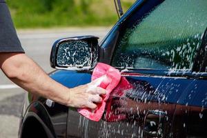 mann wäscht auto draußen. Auto von Hand reinigen. männliche hand, die rosa schwamm mit schaum hält. foto