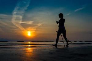 Frau, die spät am Strand bei Sonnenaufgang Nordic Walking praktiziert foto