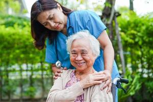arzt hilft asiatischen älteren frauen mit behinderungspatienten, die im park im rollstuhl sitzen, medizinisches konzept. foto