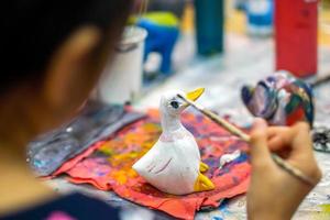 Nahaufnahme und Ernte Hände von Mädchen, die Pinsel studieren und Farbe auf Holztierpuppe im Kunstklassenzimmer ihrer Schule lernen. foto