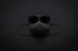 sonnenbrille und gesichtsmaske auf dunklem hintergrund für minimalistisches, flaches schwarzes konzept foto