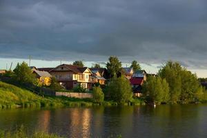 ein Dorf am Flussufer mit hellgrünem Gras und einem wunderschönen Himmel. foto