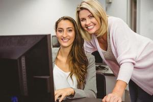 lächelnder Lehrer und Schüler hinter Schreibtisch am Computer foto