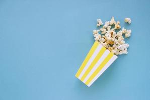 Verschüttetes Popcorn und Papiereimer auf blauem Hintergrund. Filmabend-Konzept. Platz für Text kopieren foto