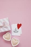 Happy Valentinstag Zusammensetzung. leeres grußkartenmodell, geschenkboxen, rote herzen, konfetti auf rosa hintergrund foto