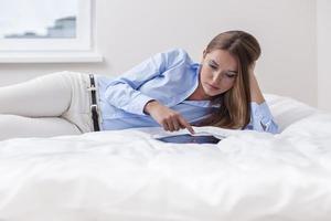 schöne Frau mit Tablet-Computer auf ihrem Bett