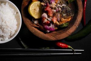 würziges gebratenes Fischmenü mit Reisschüssel auf schwarzem Hintergrund. asiatische Lebensmittelfotografie. gut für Speisekarte und Poster foto