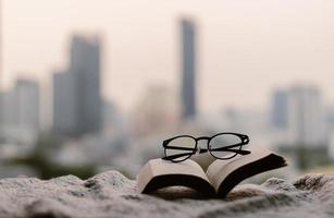 Brille und offenes Buch auf Decke im Schlafzimmer mit Stadthintergrund. foto