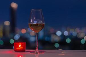 Ein Glas Roséwein mit roter Kerze auf dem Tisch und farbenfrohem Stadt-Bokeh-Lichthintergrund.