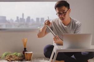 asiatischer mann in freizeitkleidung sitzt und arbeitet am laptop im zimmer foto