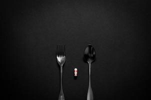 Gabel und Löffel mit einer Kapselmedizin auf dunklem Hintergrund. minimalistische flache lage schwarz für gesundheitskonzept. foto