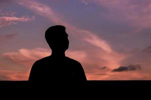 Silhouette des asiatischen Mannes bleibt allein mit abendlichem Himmelshintergrund. Konzept für Depressionen und psychische Gesundheit. foto
