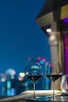 Zwei Gläser Rotwein auf dem Tisch der Bar auf dem Dach mit farbenfrohem Bokeh der Lichter der Stadt. foto