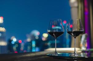 Zwei Gläser Rotwein auf dem Tisch der Bar auf dem Dach mit farbenfrohem Bokeh der Lichter der Stadt.