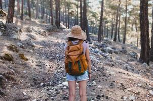 eine Frau mit Rucksack und Strohhut auf einem Bergpfad foto