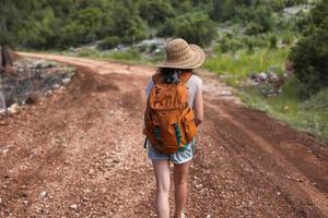 eine Frau mit Rucksack und Strohhut auf einem Bergpfad foto