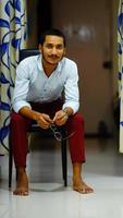 indischer junger gutaussehender mann, der zu hause auf stuhl sitzt foto