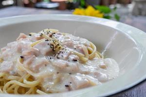 Spaghetti Carbonara, eine köstliche Mischung aus Schinken, Speck und heißem Käse, serviert in einem weißen Teller auf einem verzehrfertigen Holztisch. leckere Spaghetti mit Carbonara-Sauce gemischt mit Schinken, Speck und Käse. foto