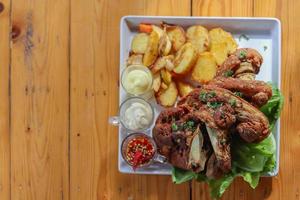 deutsche schweinshaxe wird mit gebackenen kartoffeln und sauce in einem weißen keramikteller serviert, der auf dem esszimmertisch platziert wird, um die schweinshaxe bereit für ein festliches abendessen zu machen. foto