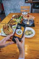 chiang mai thai 9. juli 2020 eine junge frau benutzt ein smartphone, um fotos von den speisen auf dem tisch zu machen, um sie in sozialen medien mit freunden und verwandten zu teilen, um über die speisekarte und die restaurants zu erfahren.