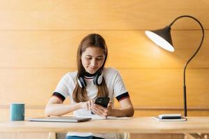 glücklicher asiate im kopfhörergebrauch laptop nehmen online kurs schulung machen notizen. lächelnde junge asiatische studentin in kopfhörern lernt von zu hause aus am computer. Fernunterrichtskonzept. foto