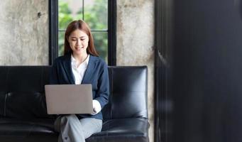 asiatische frau, die e-mail auf laptop-computer schreibt, während sie zu hause sitzt, junge geschäftsfrau, die kreatives modernes büro des starts arbeitet. Marktbestand analysieren, neue Strategie. foto