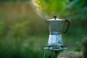 antike kaffee-moka-kanne auf dem gasherd zum camping, wenn die sonne morgens aufgeht. weicher fokus.