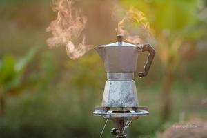 antike kaffee-moka-kanne auf dem gasherd zum camping, wenn die sonne morgens aufgeht. weicher fokus. foto