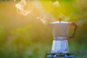 moka pot und rauch, kaffee sonnen sich auf feuer, im wald bei sonnenaufgang am morgen. weicher Fokus. flacher Fokuseffekt.