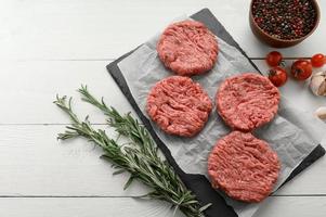 Raw Beef Burger Patties auf Metzgerholzbrett, Rosmarin und Pfeffer. schwarzer Hintergrund. Sicht von oben. foto