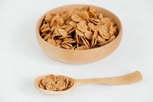 Knusprige, gesunde, trockene Getreideflocken in einer Holzschale mit Holzlöffel auf weißem Hintergrund foto