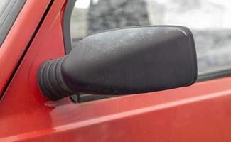 Seite links schwarzer Kunststoff-Rückspiegel auf einem roten Auto. Außenspiegel auf der Fahrerseite eines alten Autos. foto